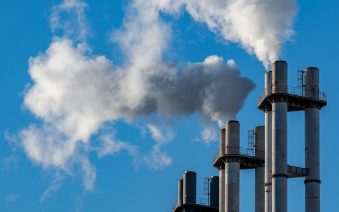 Smoke billows from industrial chimneys against a blue sky